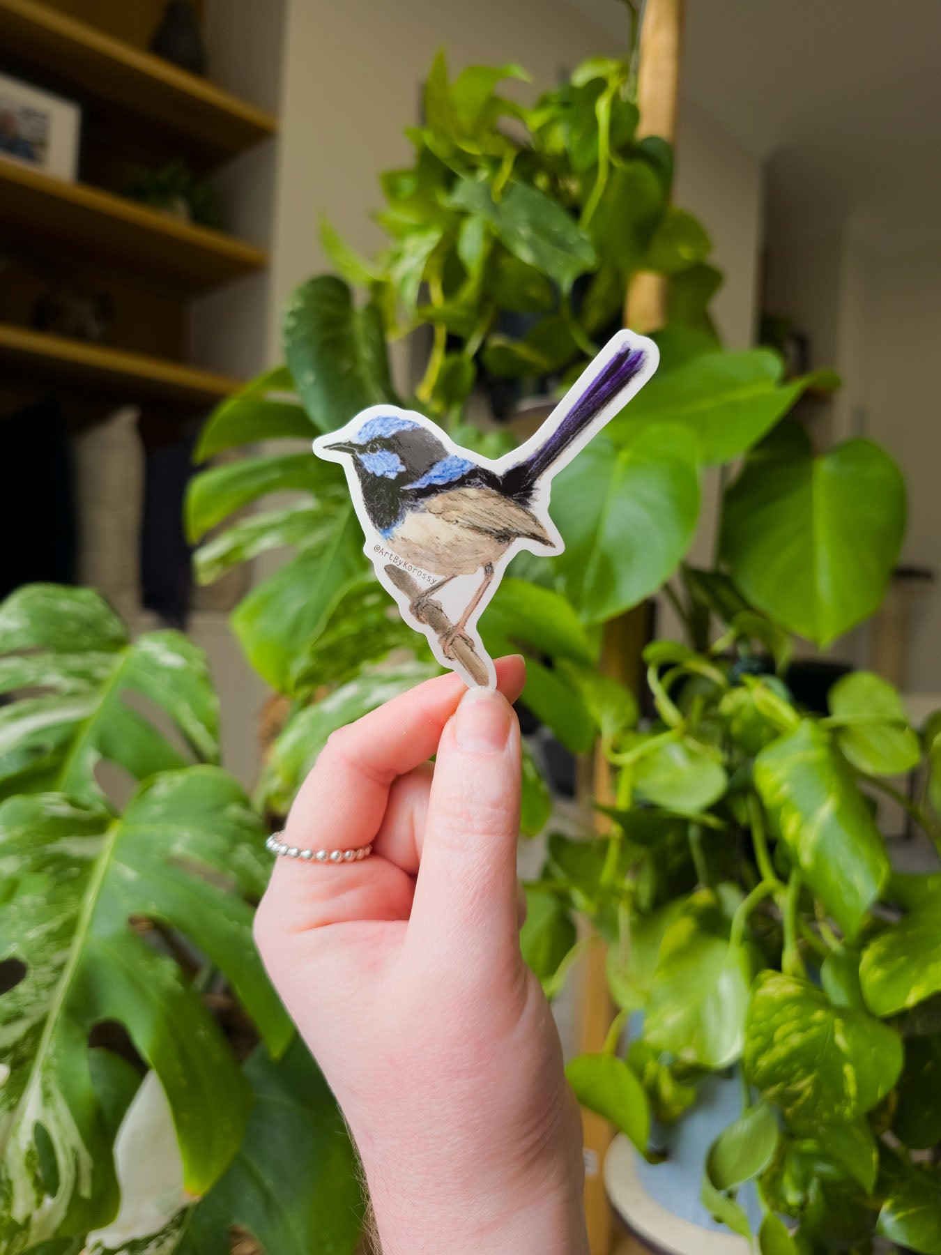 Hand holding a bird-shaped sticker in front of green plants