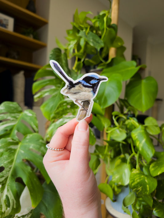 Hand holding a bird sticker in front of green plants