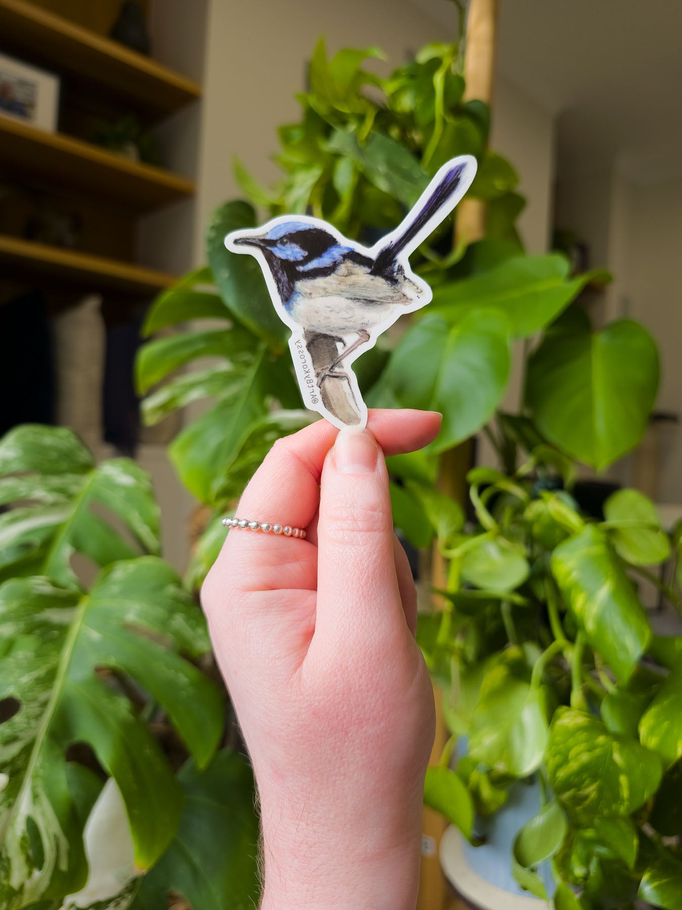Hand holding a small bird sticker in front of green plants